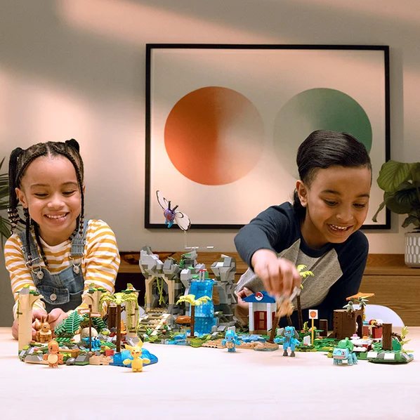 Two kids building a MEGA Pokémon scene together on a table